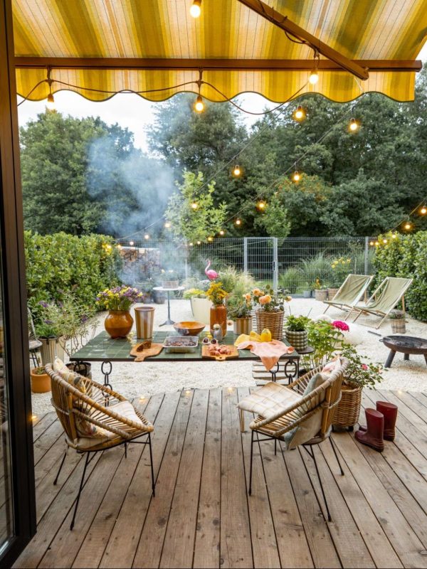 Wooden deck with a patio cover overhead with two open glass doors, a table, chairs, and twinkle lights.