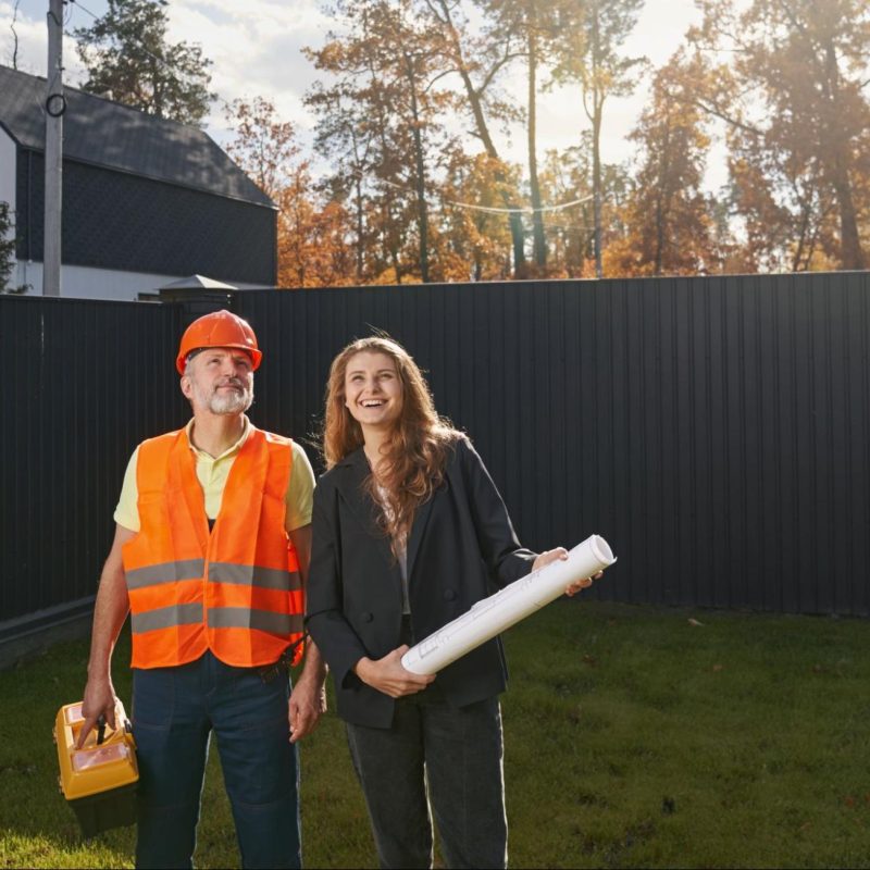 Woman and a man in a hard hat next to a privacy fence.