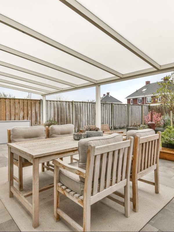 A well-designed covered patio with a cozy seating area facing a lush garden, featuring a portable BBQ grill on the side.