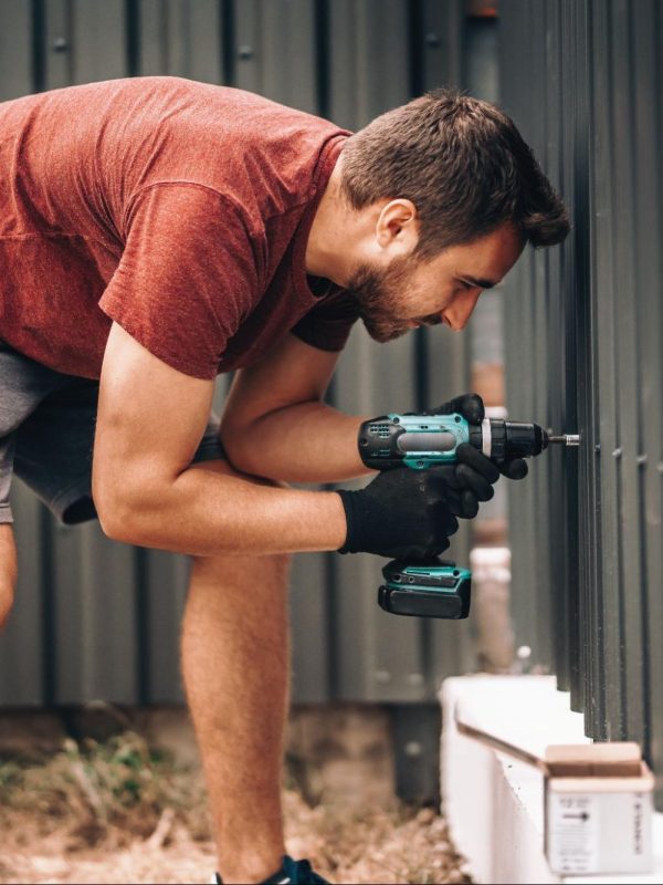 A man uses a cordless screwdriver to fasten screws on a black vinyl fence.