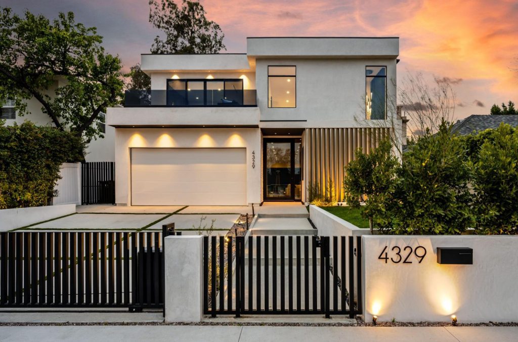 A modern two-story house with a lush garden at sunset, enclosed by a sleek black steel fence for security and style.