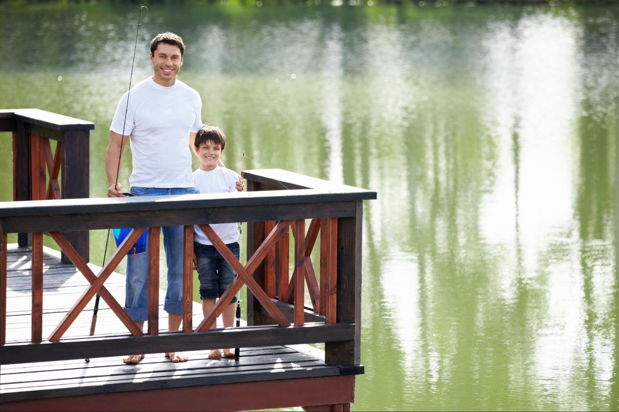 A picture of father and son near the waters of the fishing pond secured by railings.