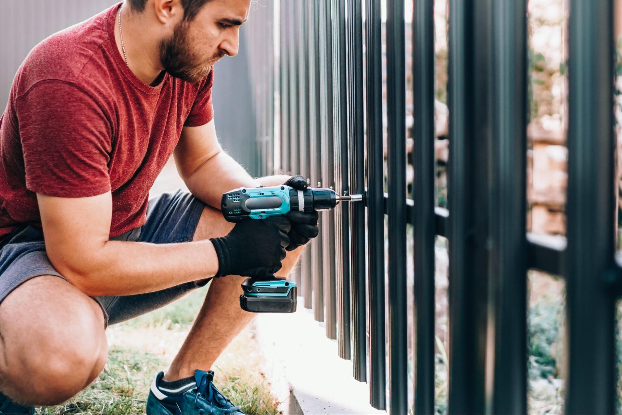 A worker focused on installing the fence using an electric screwdriver.