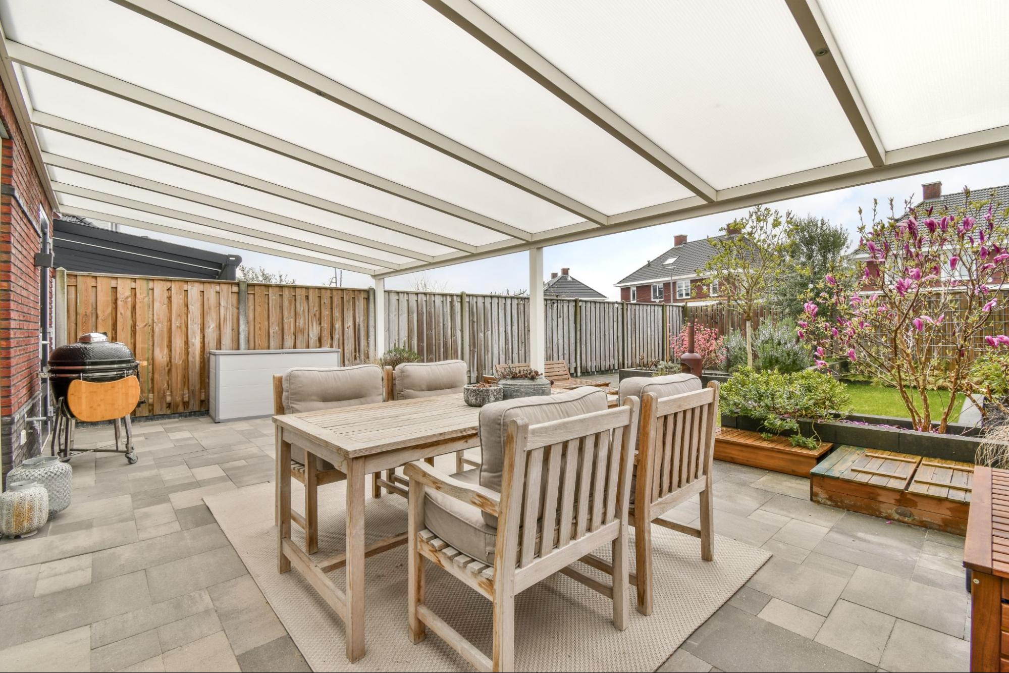A minimalist design patio brings a cozy vibe with a table and chairs and a barbeque grill surrounded by plants.