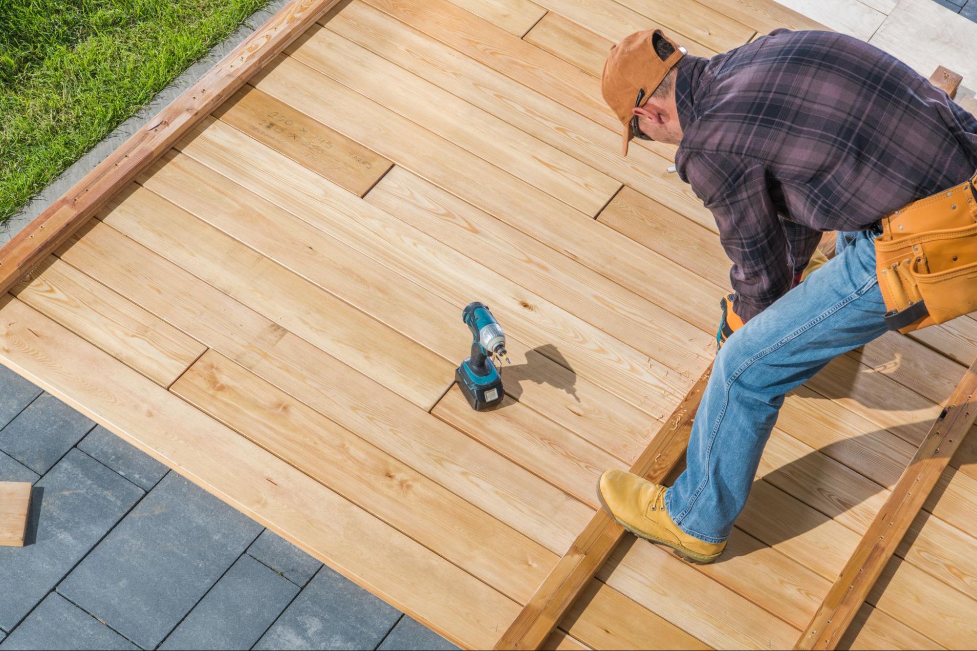 A worker is building a wooden deck outdoors.