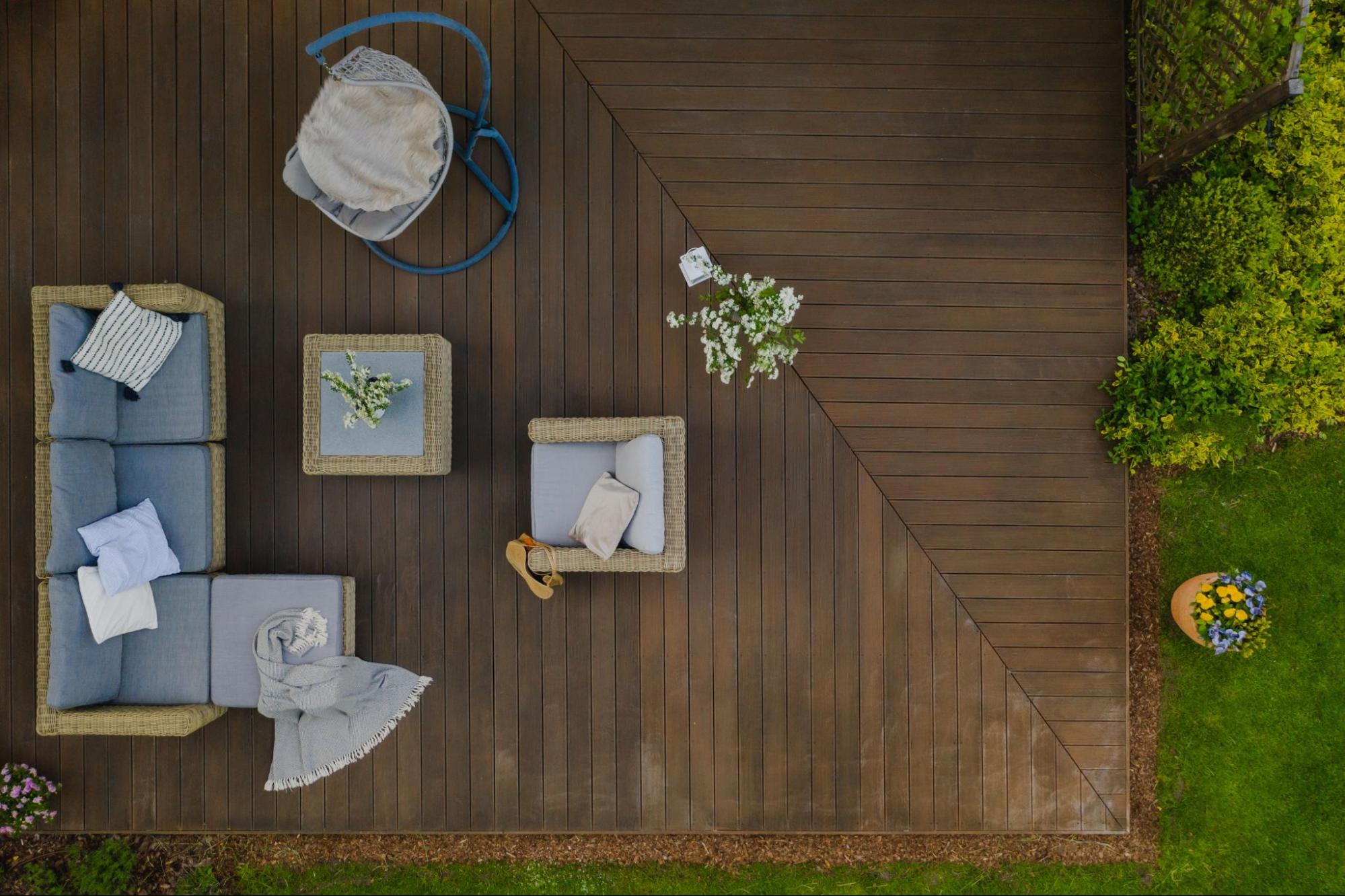 A top view of a wooden terrace with furniture surrounded by plants.