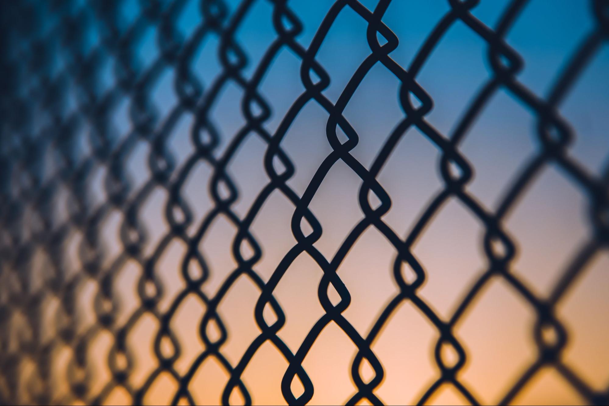 Close-up of a chain-link fence silhouetted against a blue and orange sunset sky.