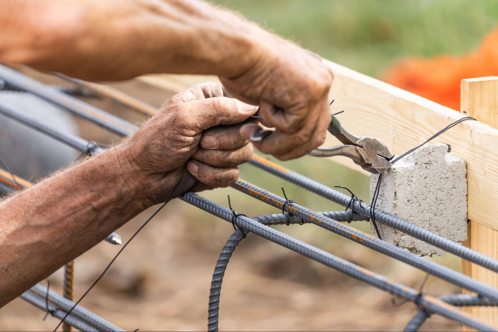 A worker securing steel rebar framing with a wire plier cutter.