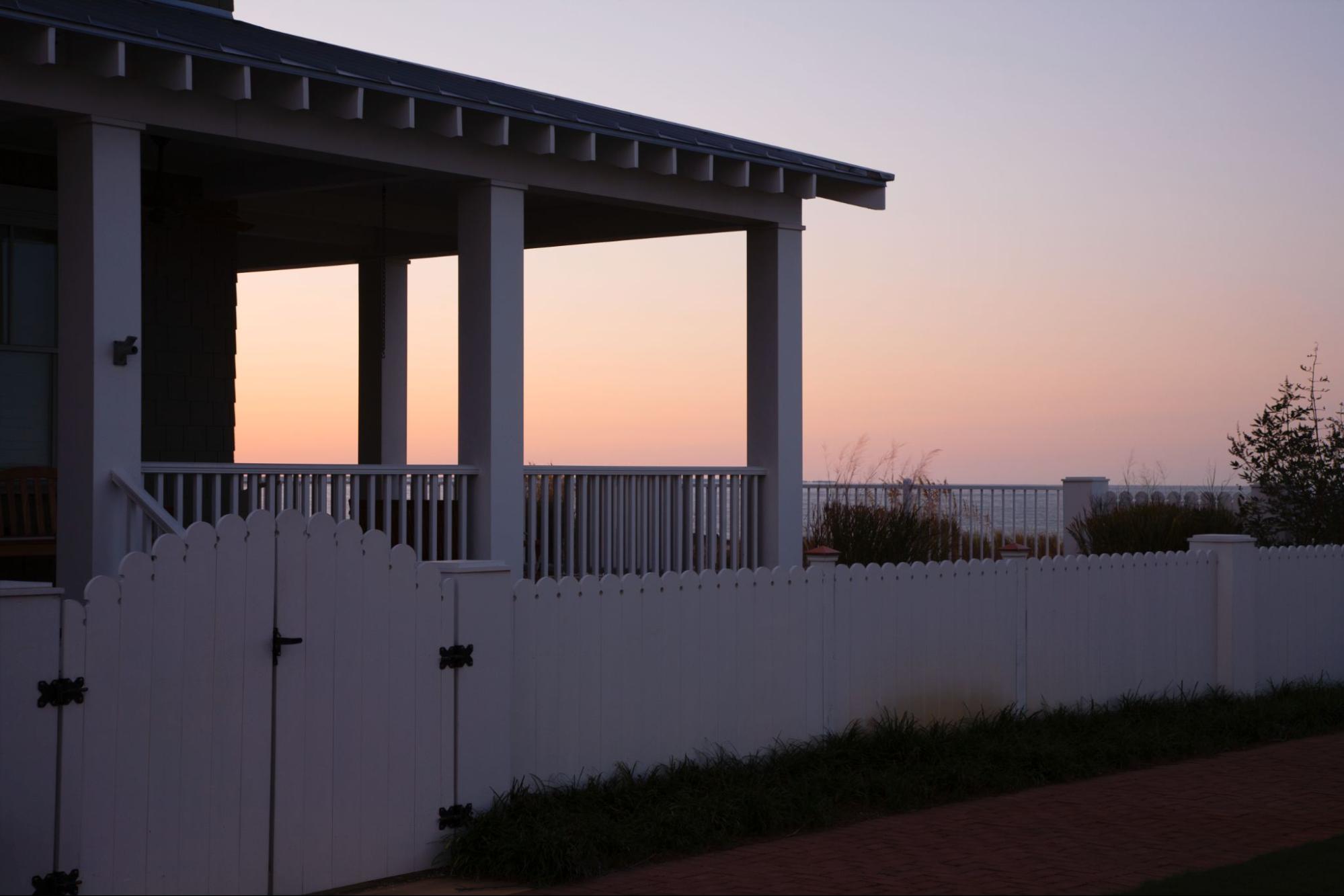 An image of white vinyl gates with fences and a covered porch in the background during sunset.