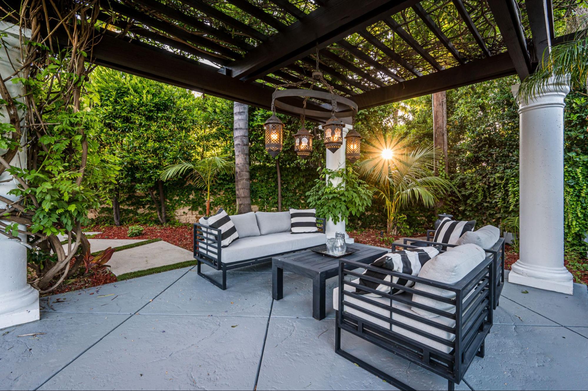A patio featuring a black and white cushioned sofa set, surrounded by lush plants and sheltered by a black steel-framed acrylic cover.