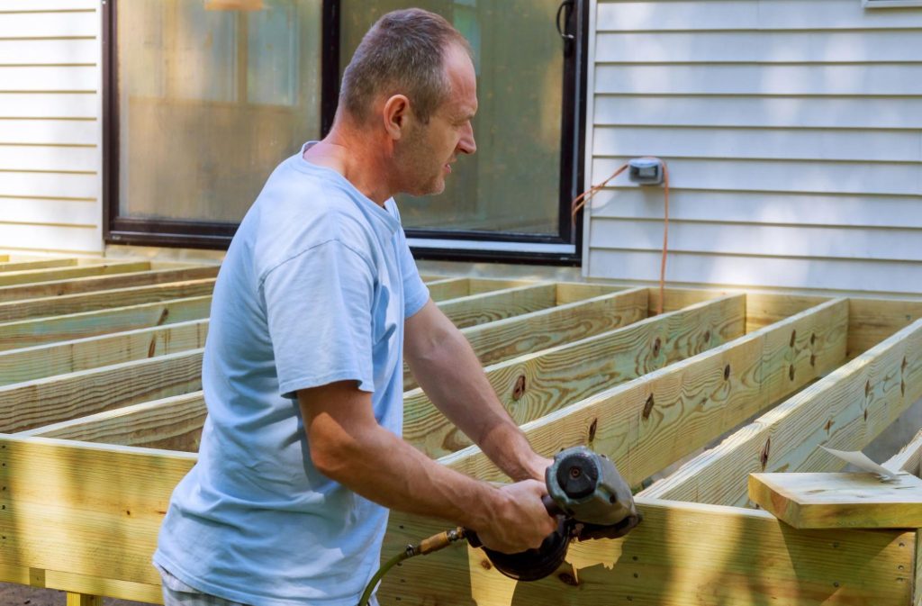 An adult man installing a wooden deck patio.