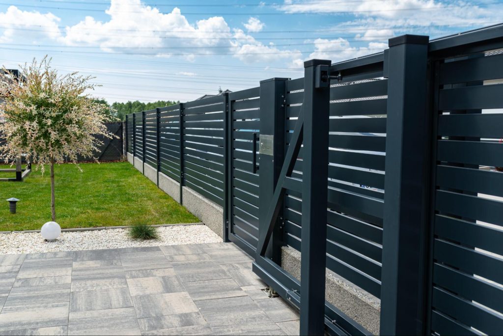 A modern panel fence in anthracite color, featuring a sliding gate leading to a garage and a matching pedestrian wicket gate, set in a stylish residence,