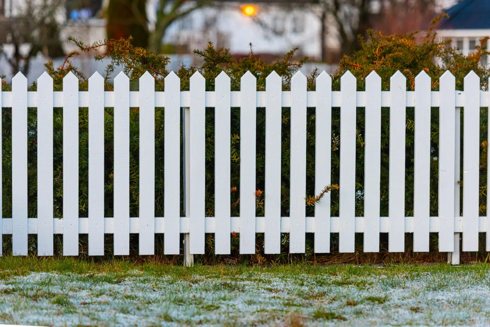 A close-up of white vinyl picket fences in front of a property.