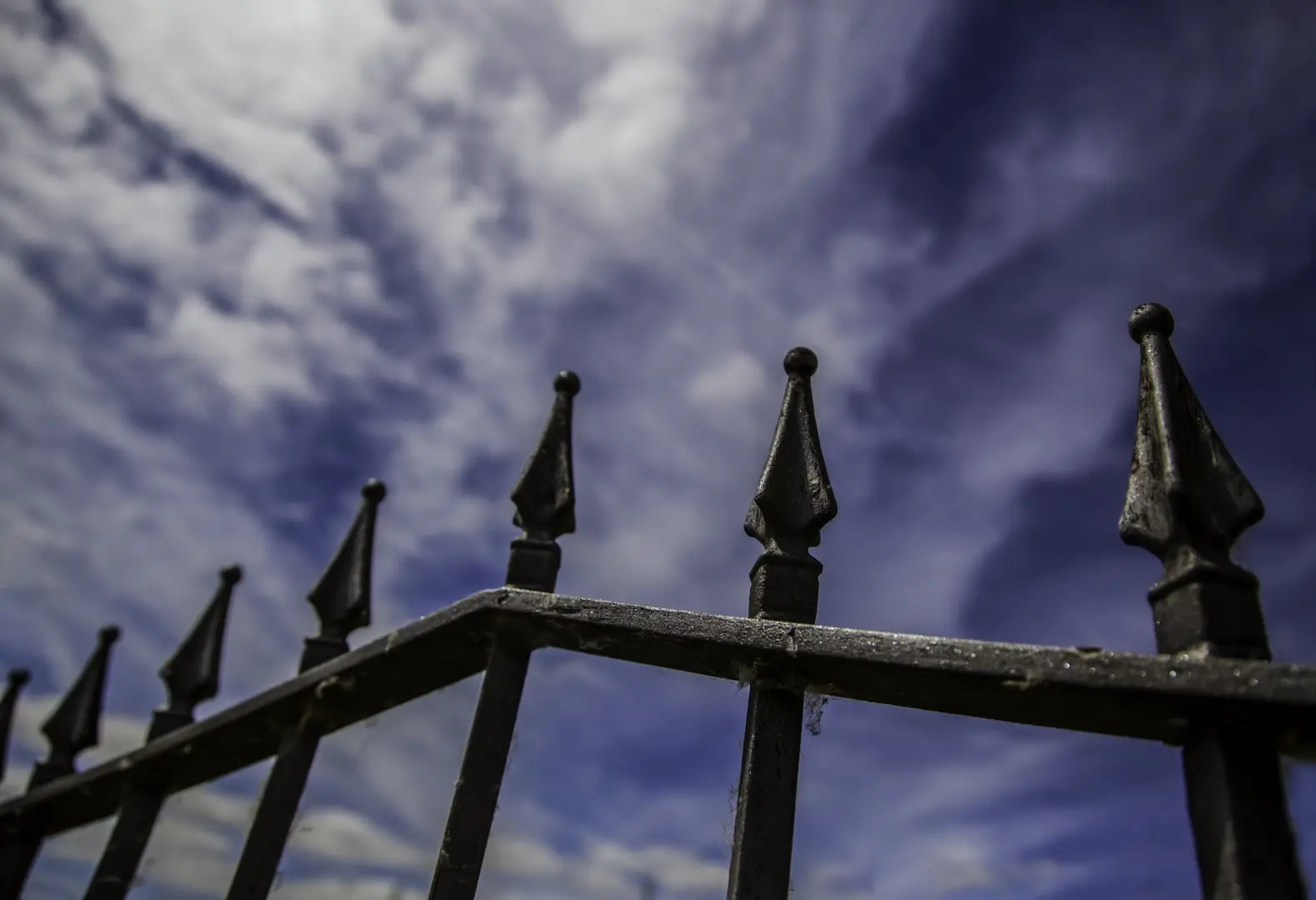 A cropped image of a pair of black gates with dark clouds.