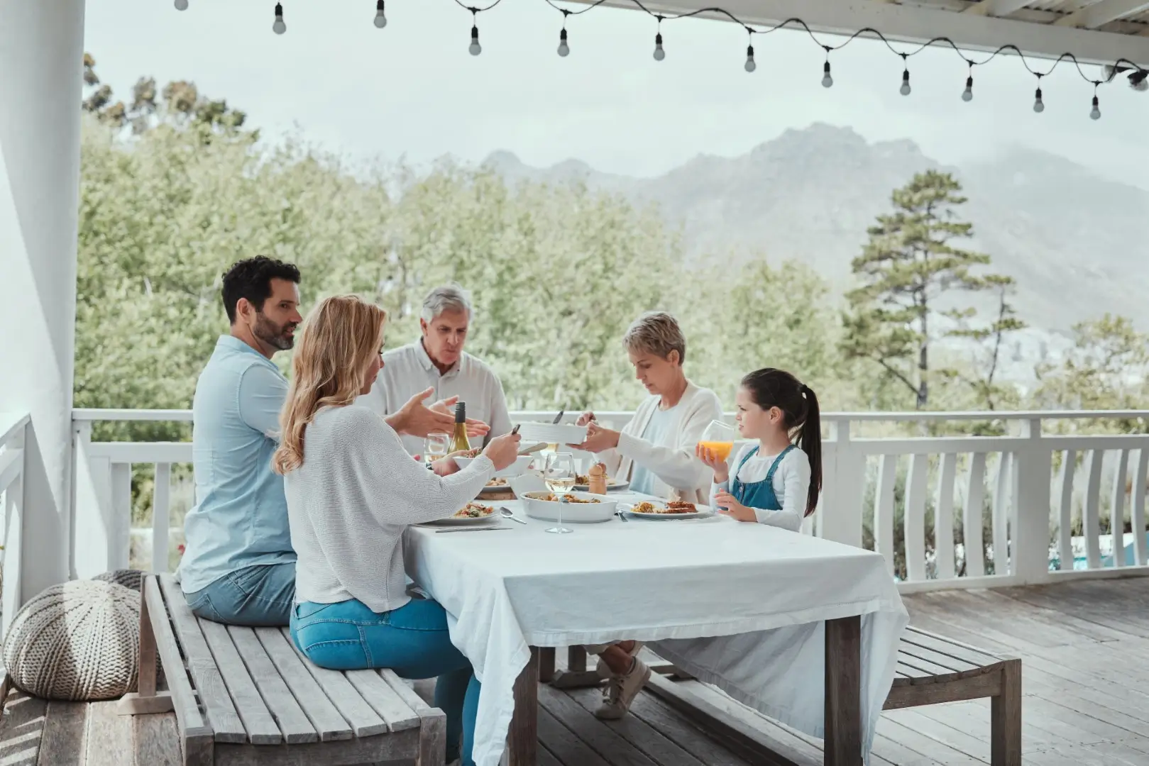 A family enjoys a meal on a covered patio, with a lush garden as a backdrop on a sunny summer day.