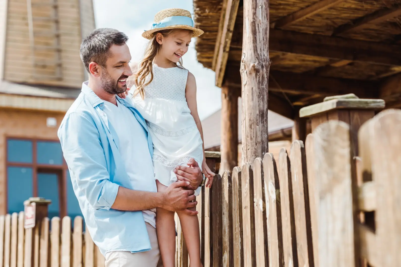 A father and daughter leaning on a wooden outdoor gate.