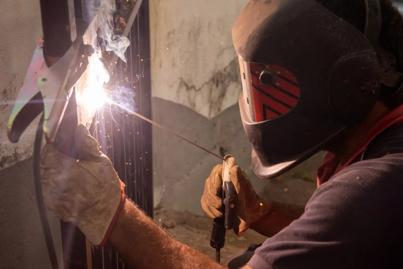 A male welder wearing a safety mask welds the steel fence.