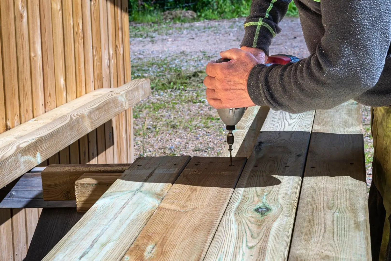 A man uses a power drill to secure a wooden deck panel during repair work.