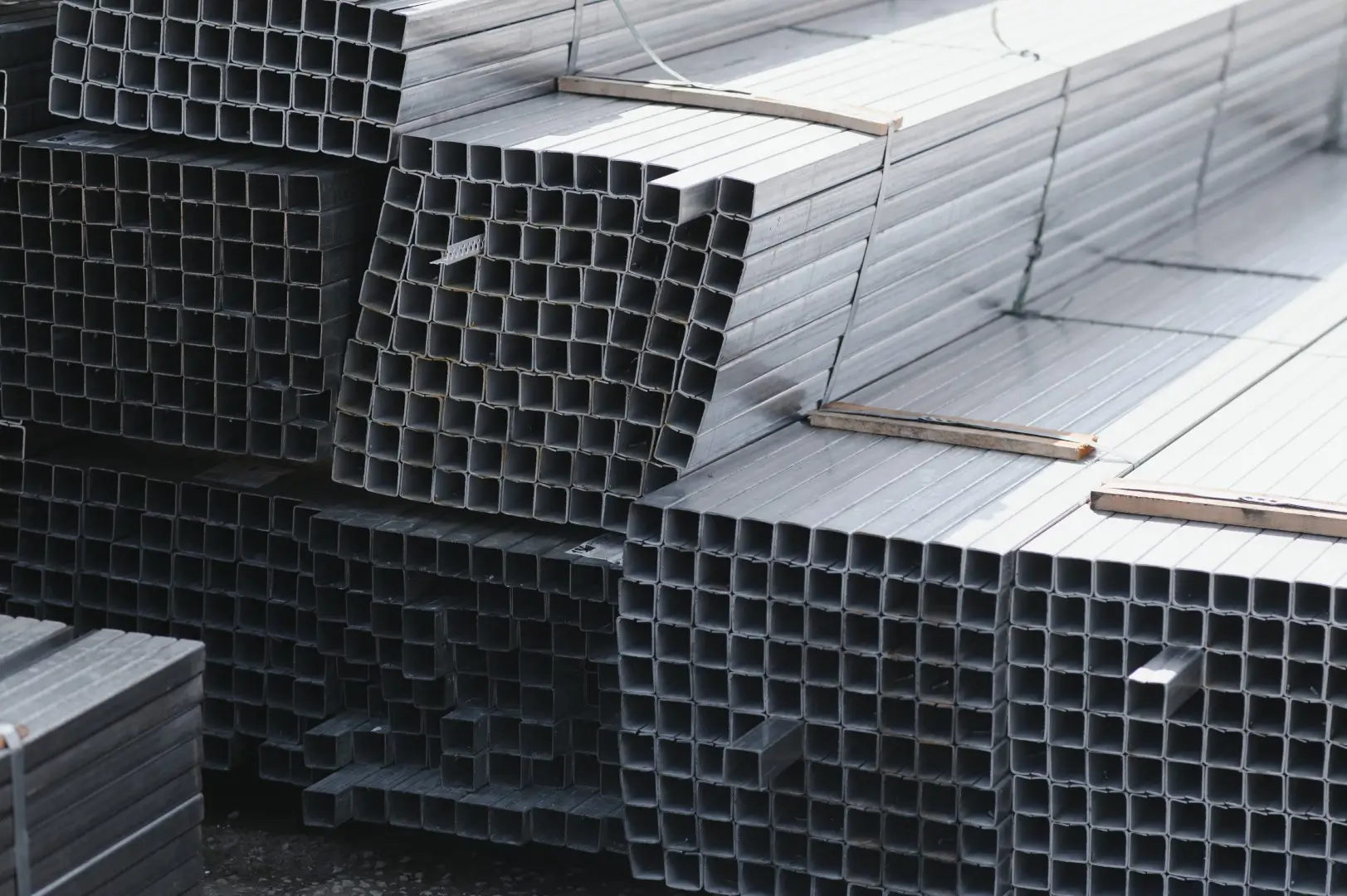 A neatly stacked pile of square galvanized steel pipes.