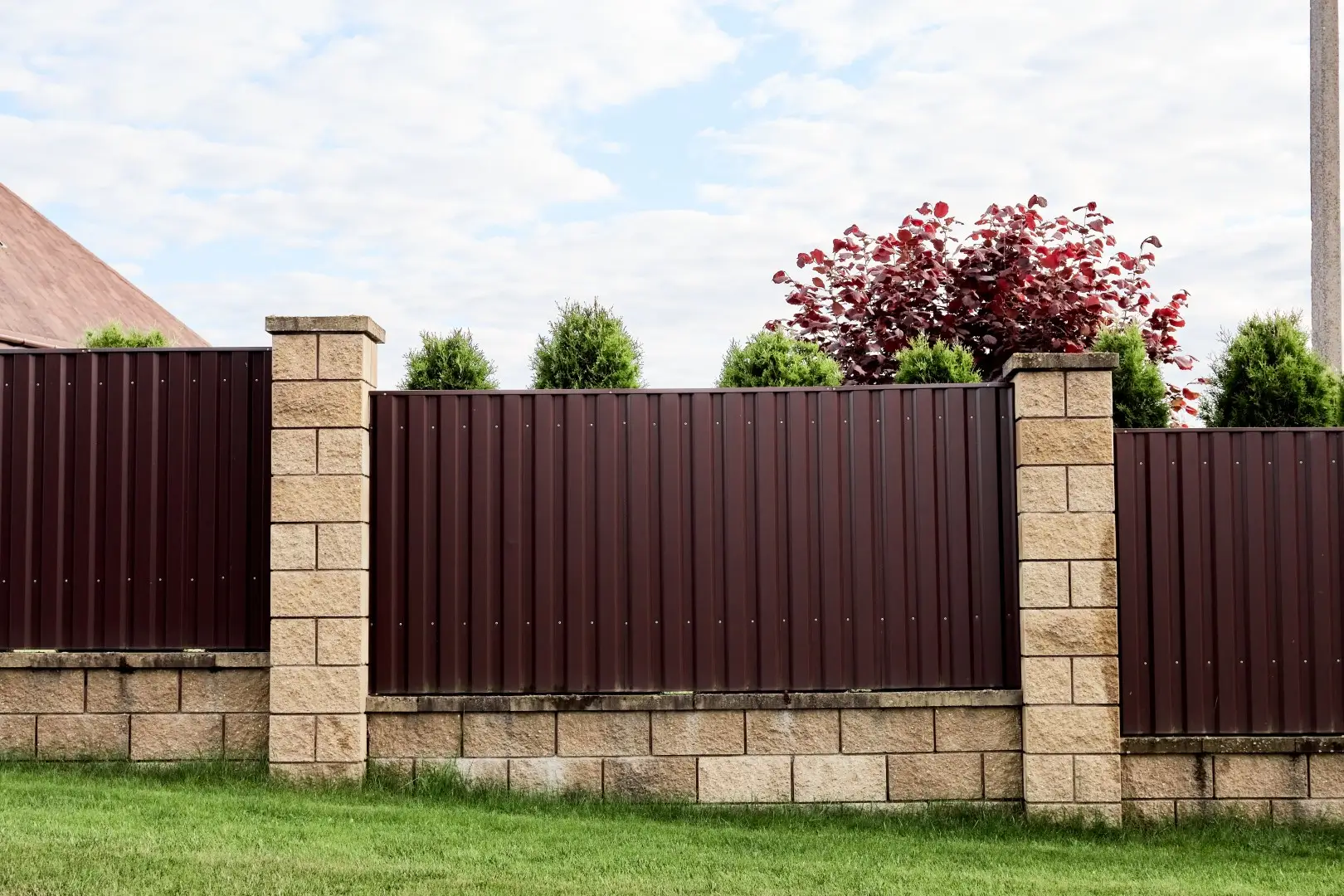 A row of vertical galvanized steel fence posts shimmering under the bright sunlight, reflecting a matte metallic finish.