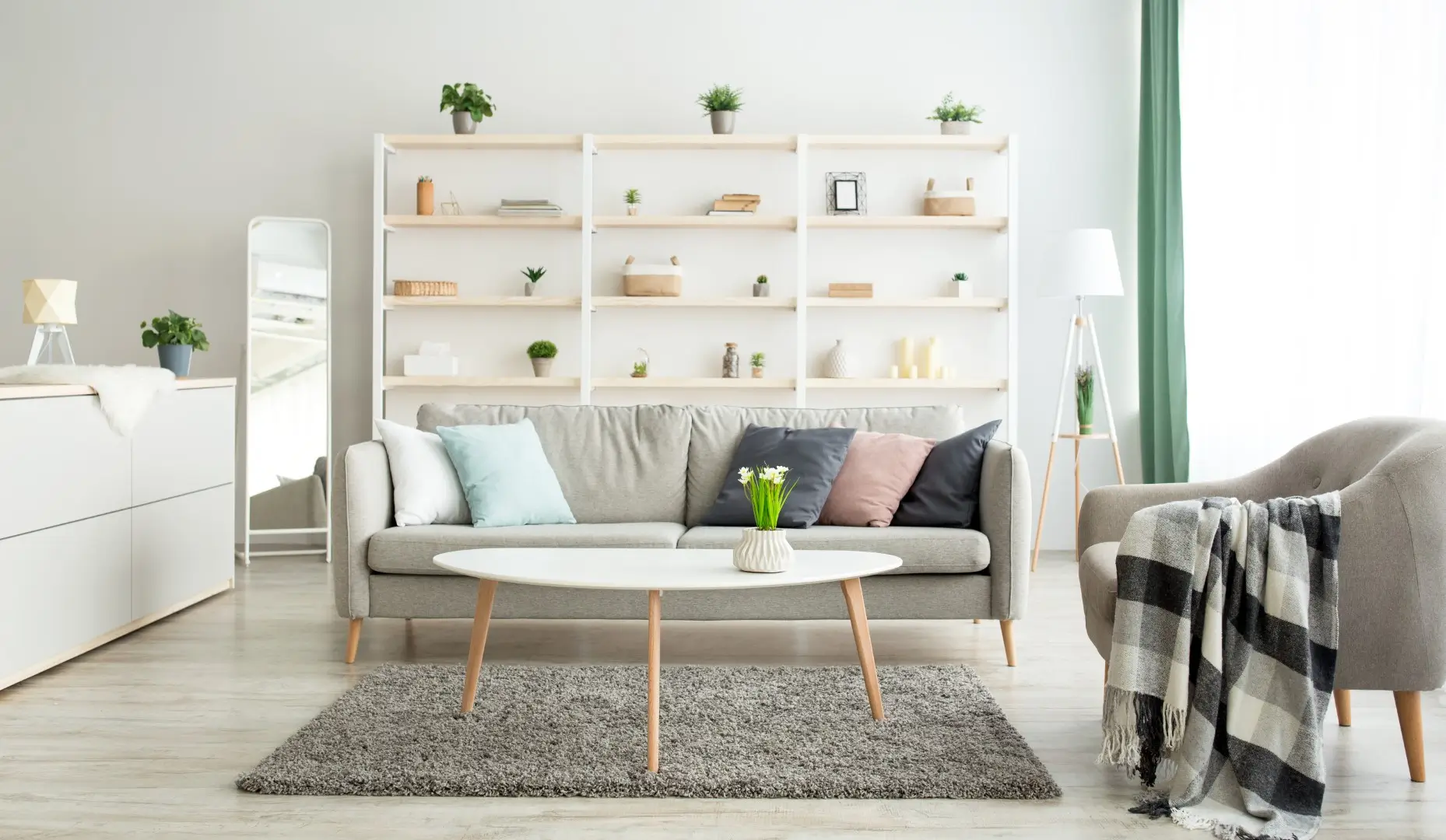 A white and gray themed living room with multi-functional spaces, featuring sleek and modern furniture such as open bookshelves, slatted cabinets, a table, lounge chairs, and tall lamps.