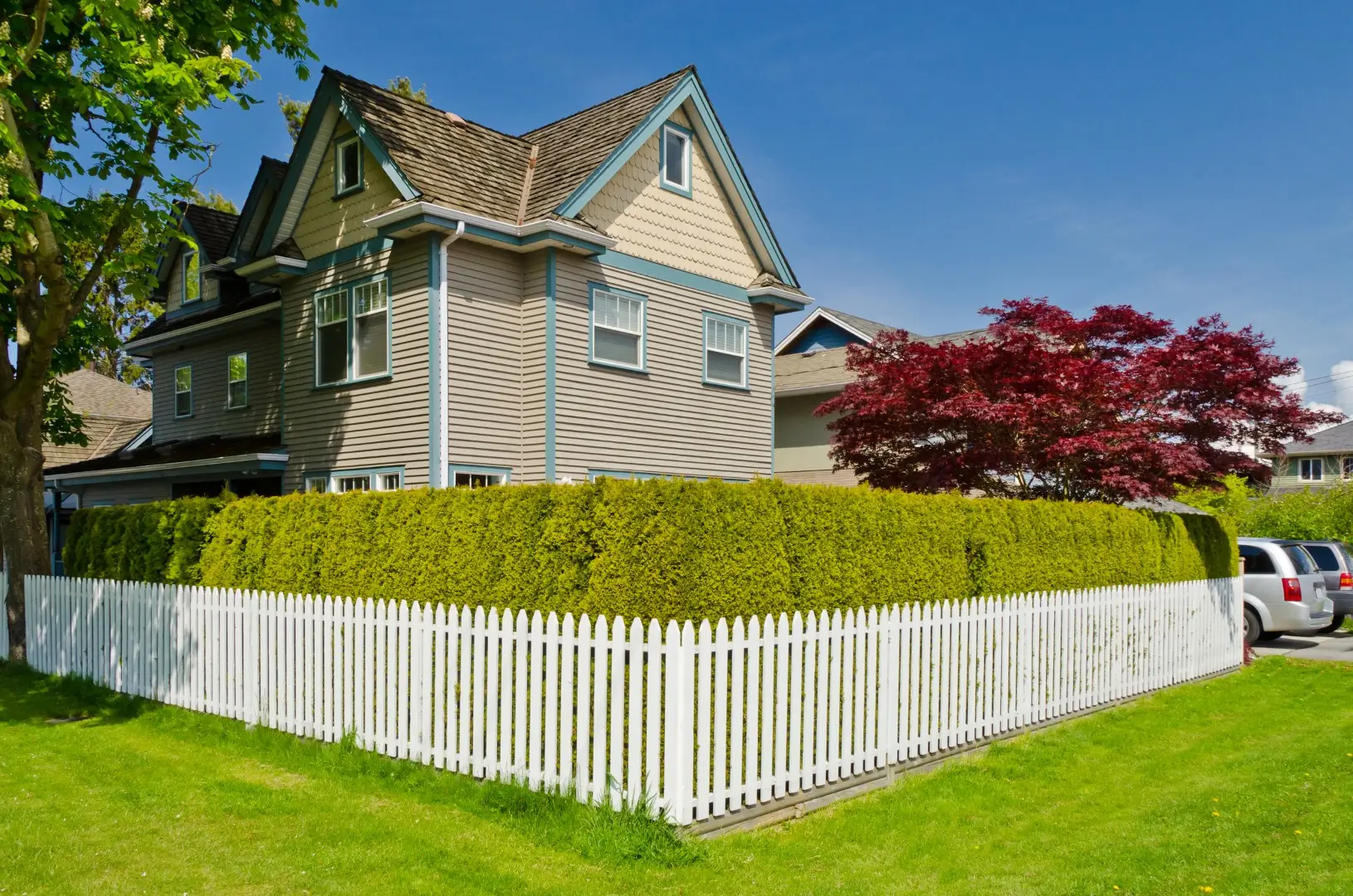A white vinyl picket fence encloses a house from the backyard's lush green lawn, defining the property's boundaries.