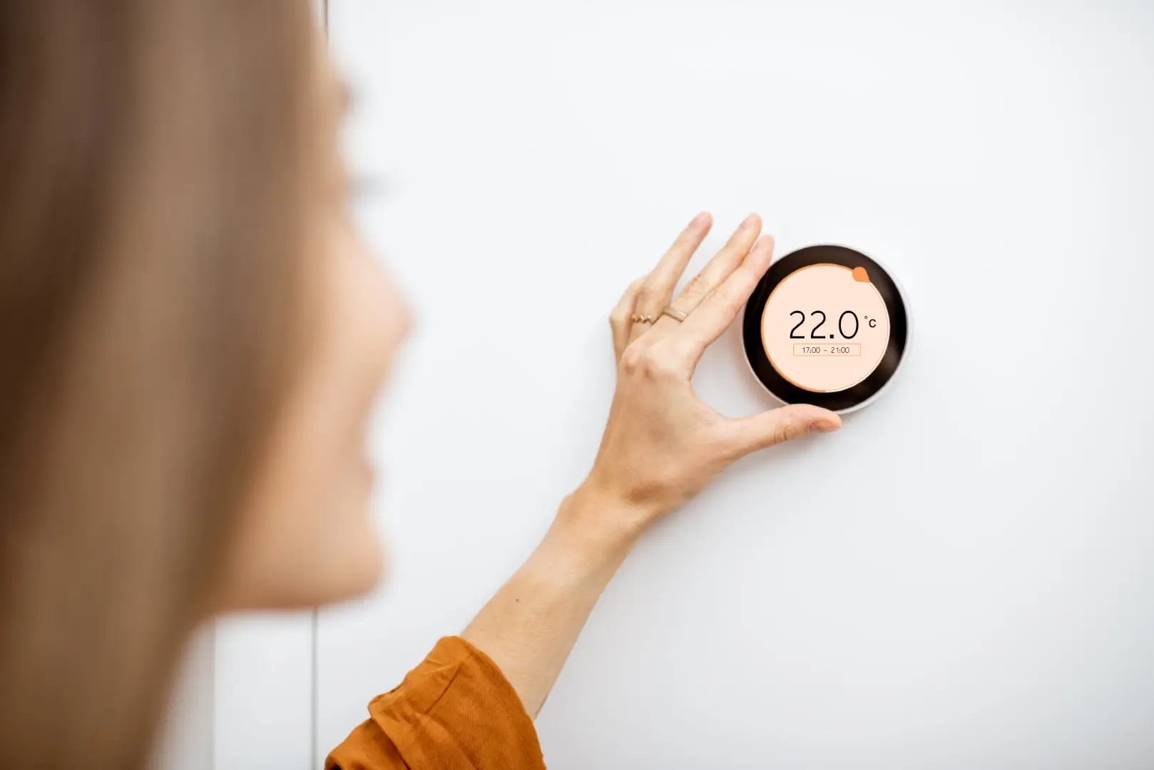 A woman's hand seamlessly adjusting the thermostat setting on a wall-mounted digital app using smart technology.