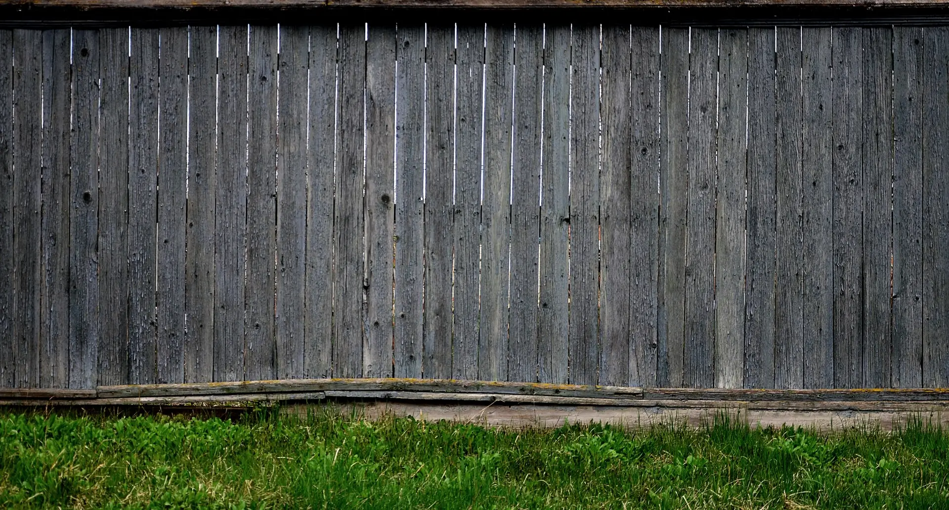 A wooden fence with grass growing near it.