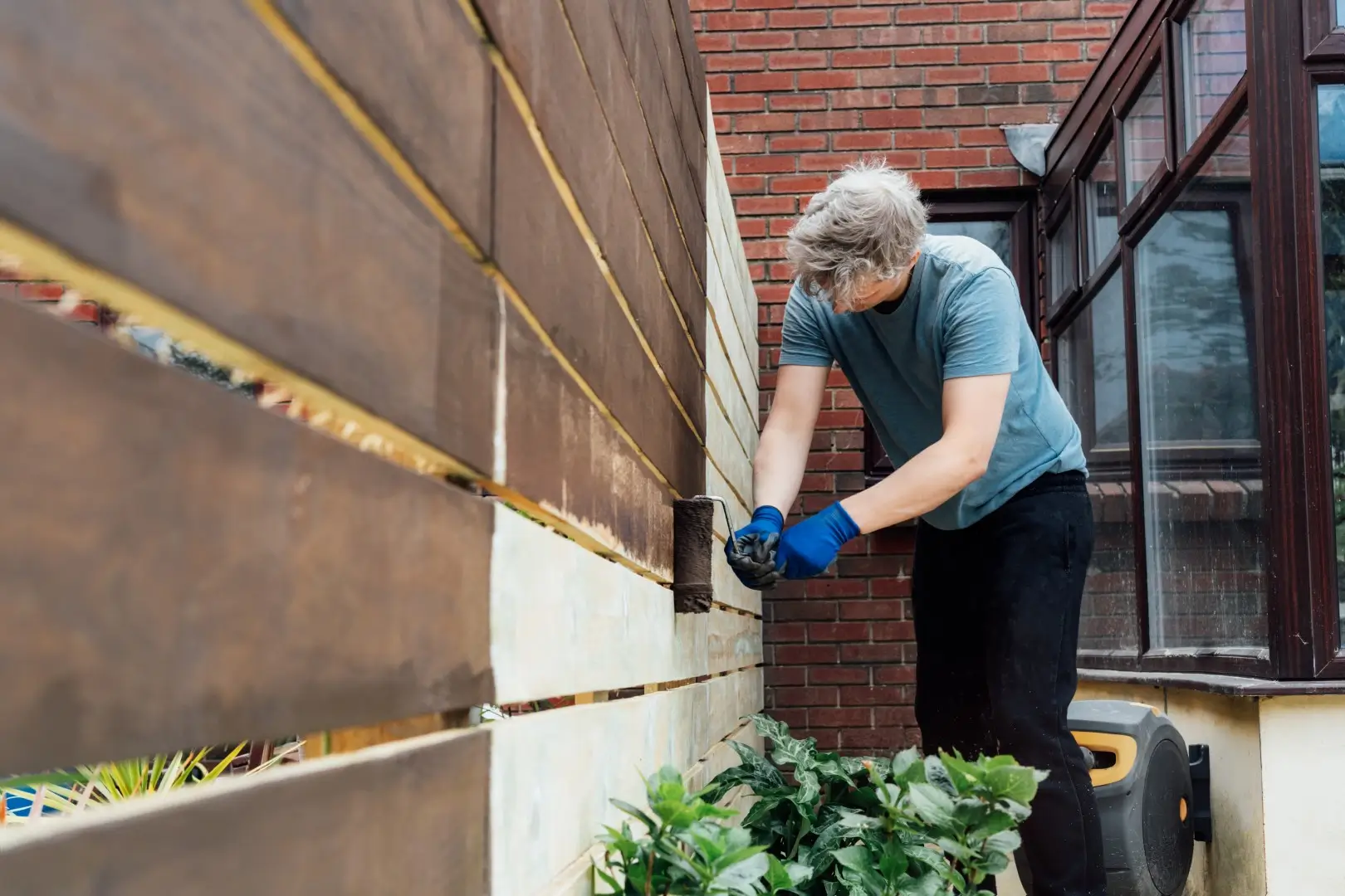 A young man paints a wooden fence with a roller.