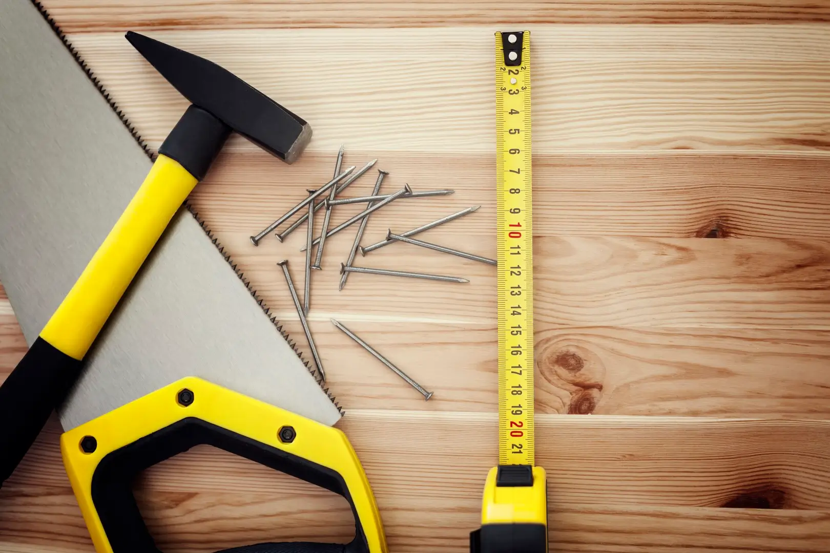 Hammer, nails, saw and tape measure on wood.
