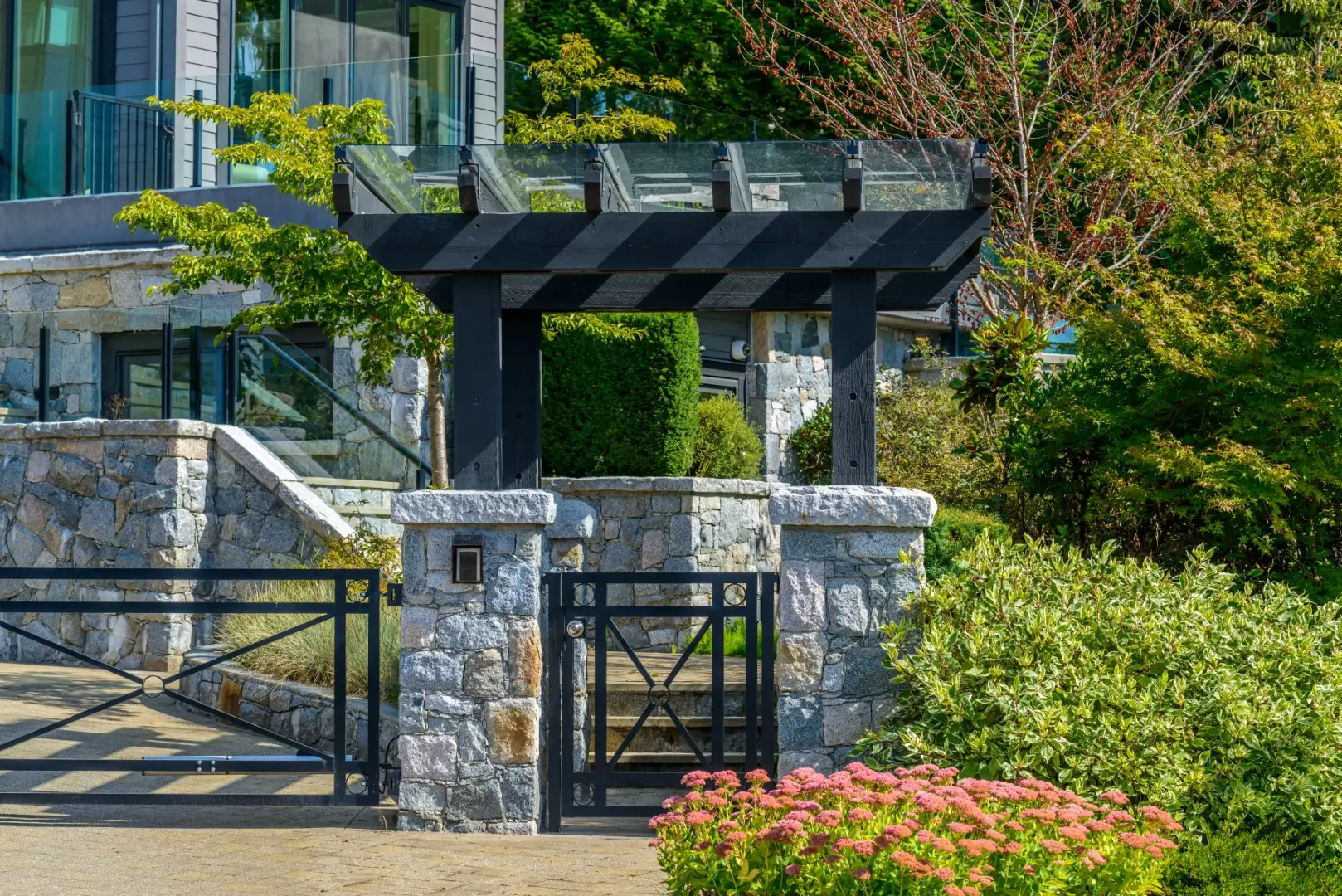 Modern black gates are securing a home. In the background is a forest.