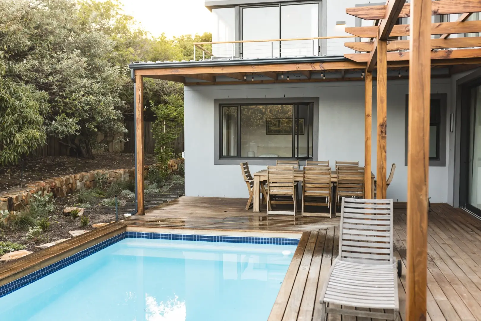 Outdoor patio with wooden furniture and swimming pool, modern home setting.