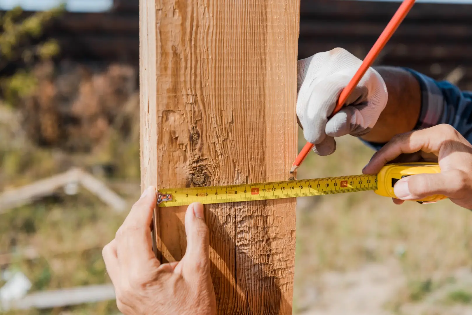 Two people measuring a fence using a pencil and a tape measure.