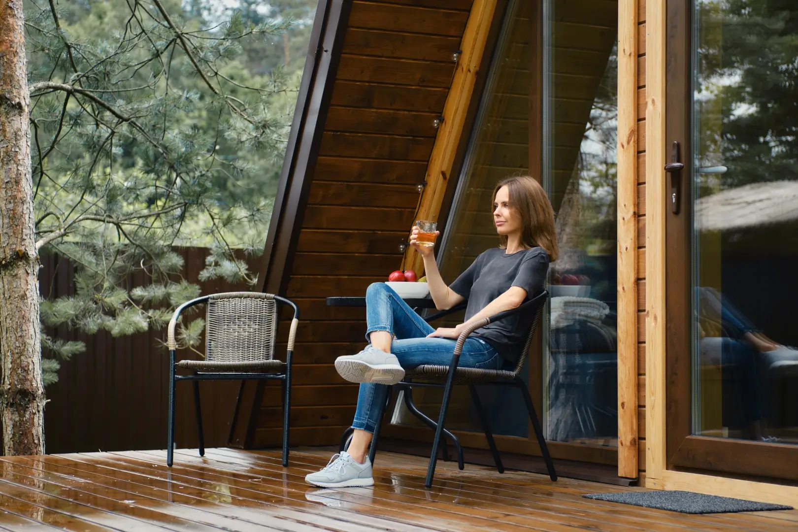 Woman sitting on a chair on a wooden deck with a glass sliding door behind her.