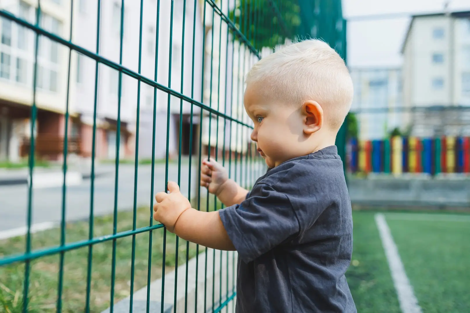 Young boy a playground surrounded by aluminum fencing.