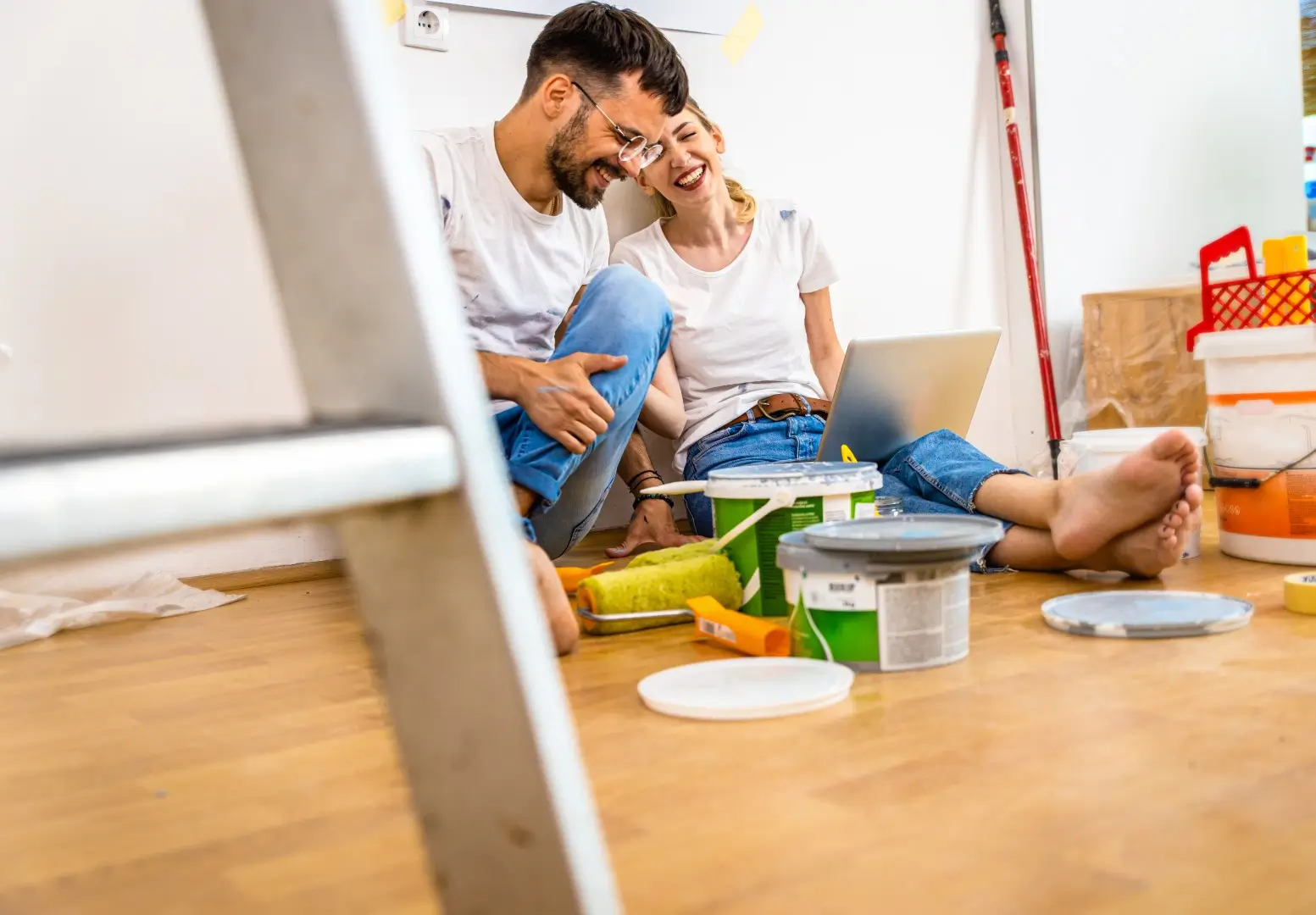 Young couple sitting on the floor choosing color via laptop for painting the wall in their home.