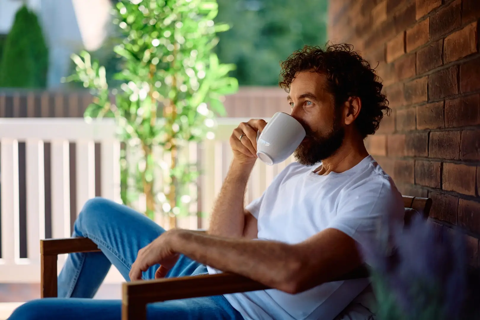 Adult man drinking coffee while relaxing on the porch.