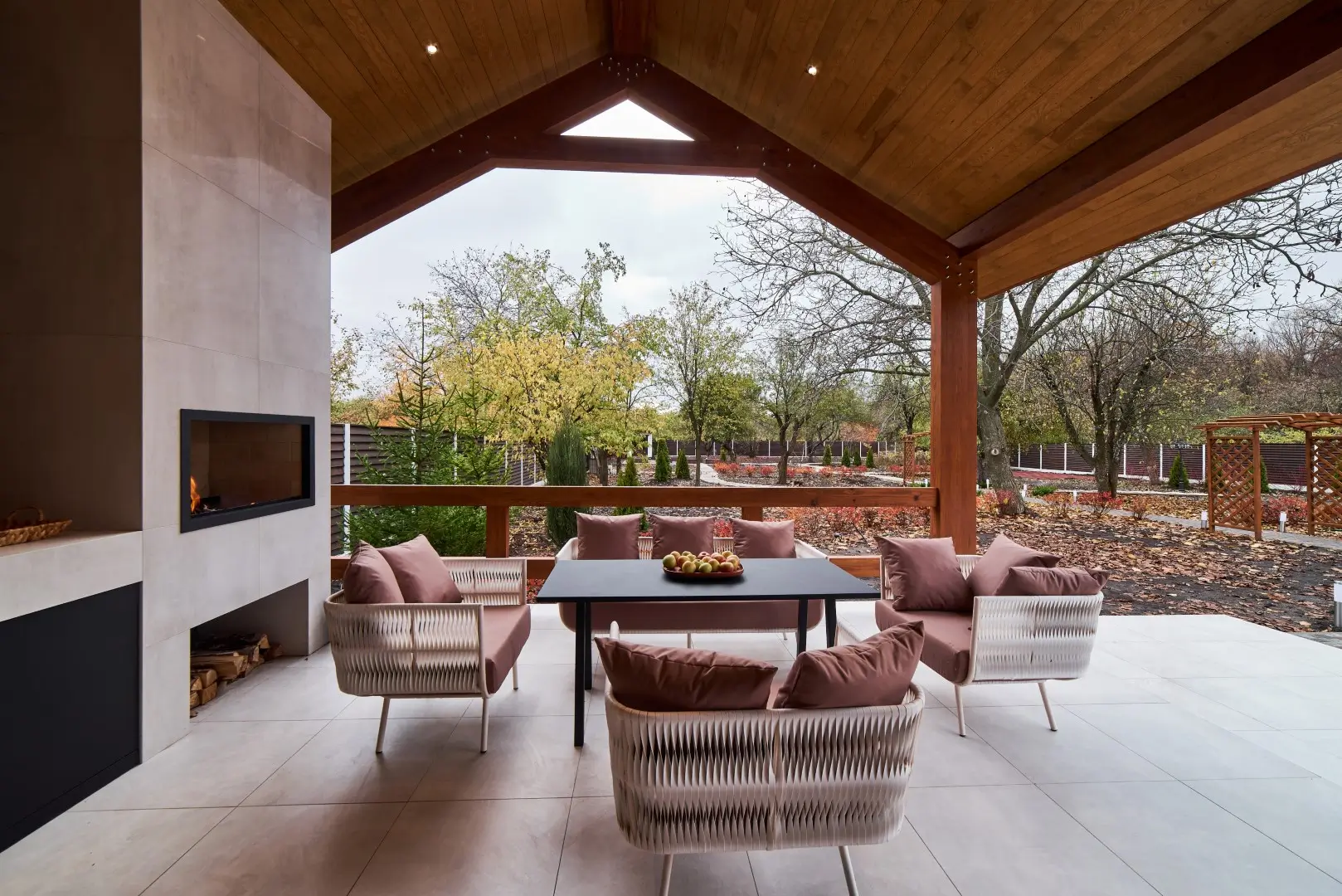 An open terrace with table, chairs, fireplace and apples.