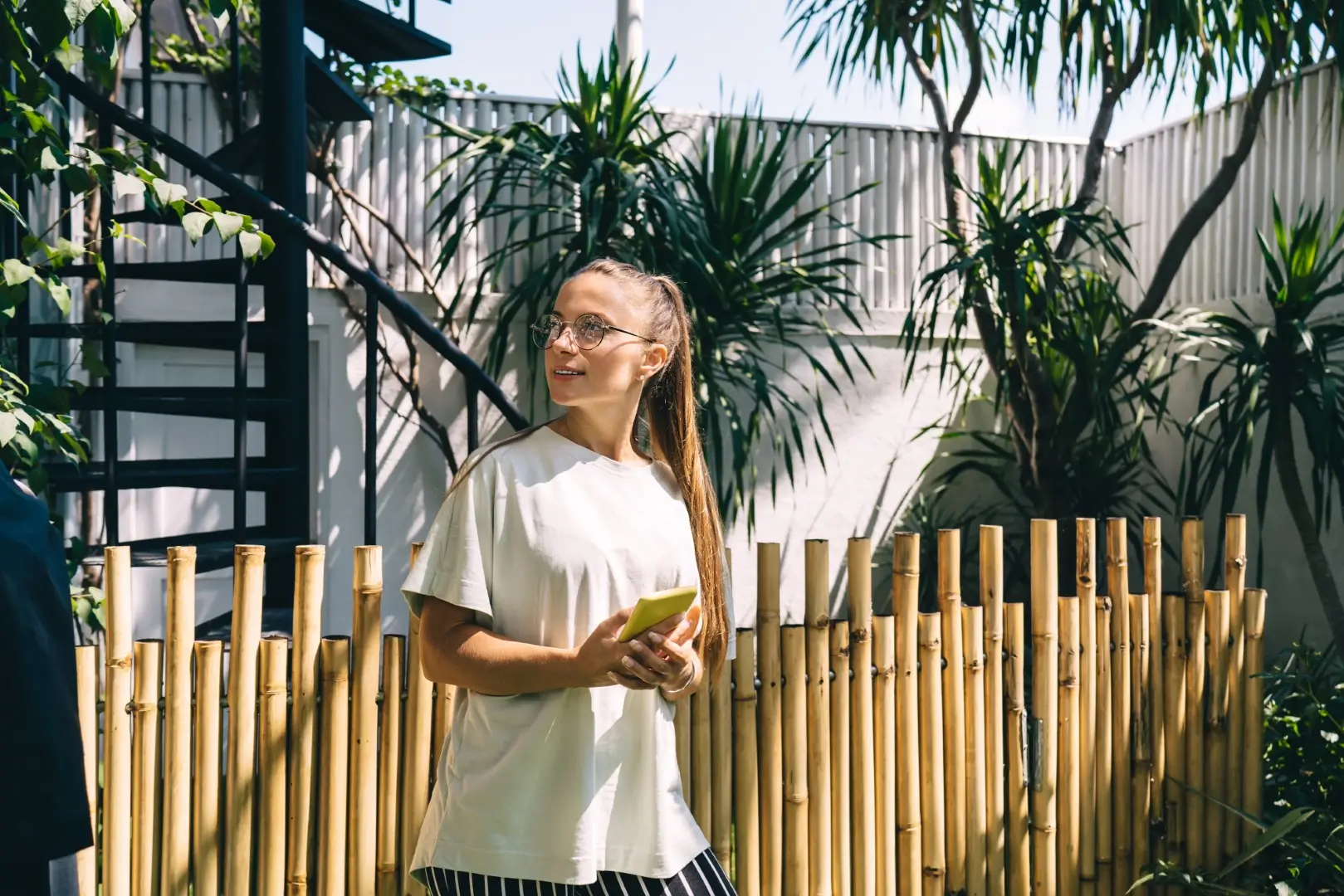 Girl casually leaning on a bamboo fence in a natural outdoor setting.