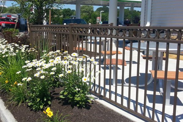 A gas station with a fence adorned by flowers and benches in the foreground.