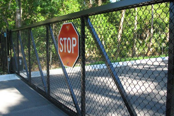 Stop sign mounted on a steel fence with trees in background.