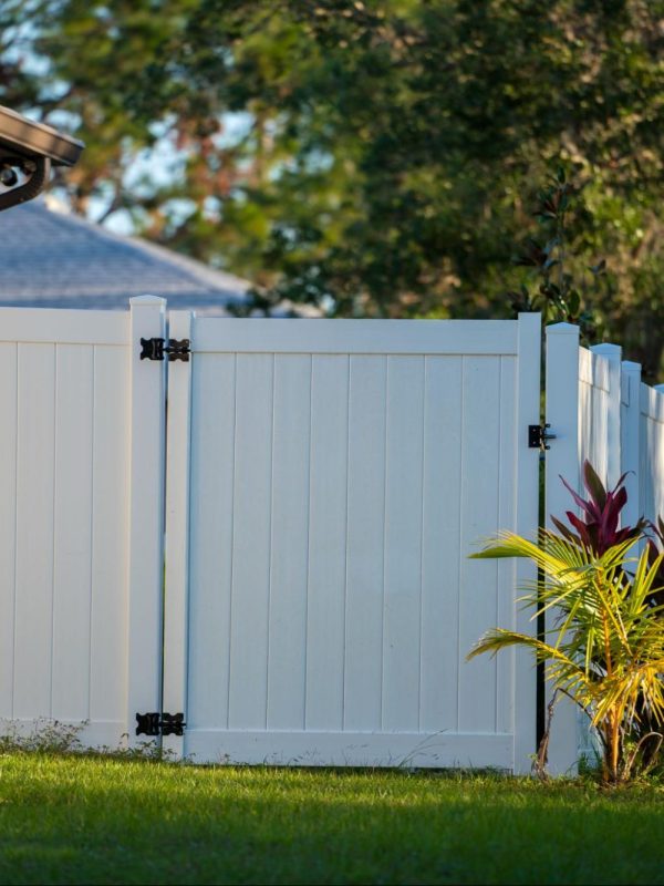 Vinyl gate on a long driveway with grass and greenery. 