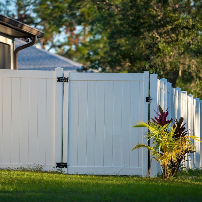 Vinyl gate on a long driveway with grass and greenery. 