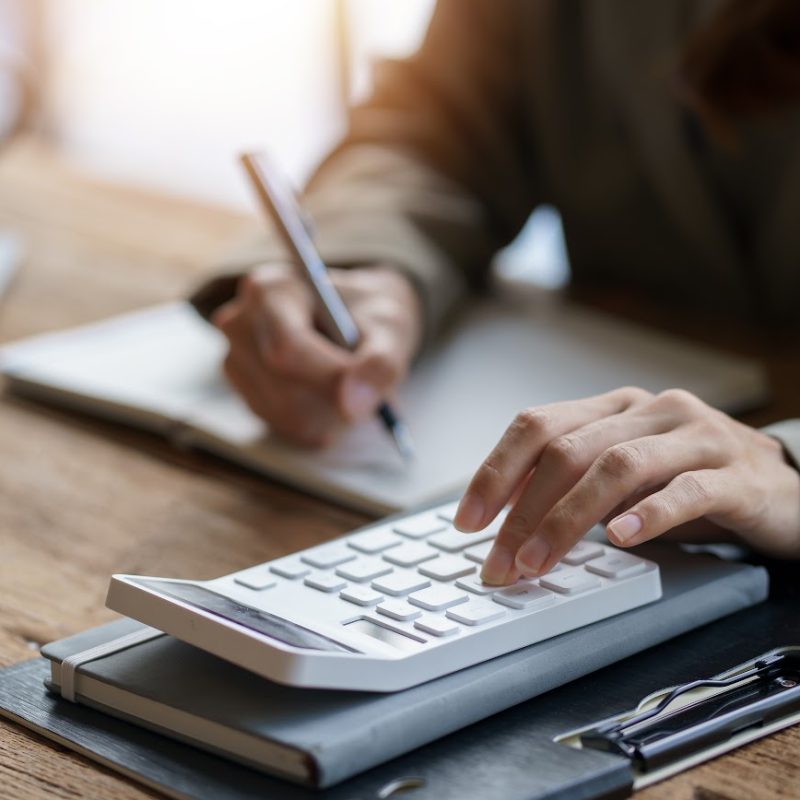Close-up of businesswoman hands using a calculator to check company finances and earnings and budget. Business woman calculating monthly expenses, managing budget, papers, loan documents, invoices.