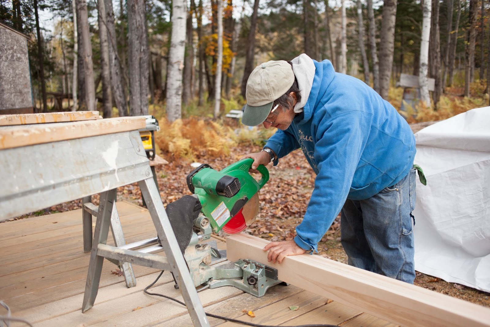 A deck builder cutting a wooden plank with an electric saw outside a home during deck construction