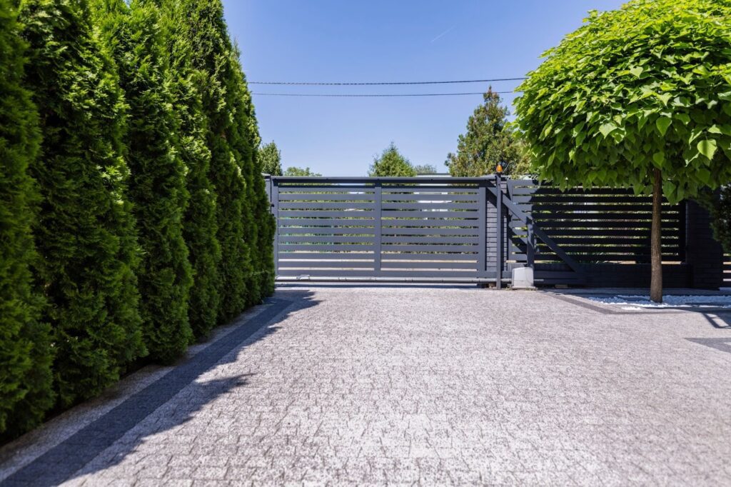 Gray fence surrounded by green trees at a residential property entrance