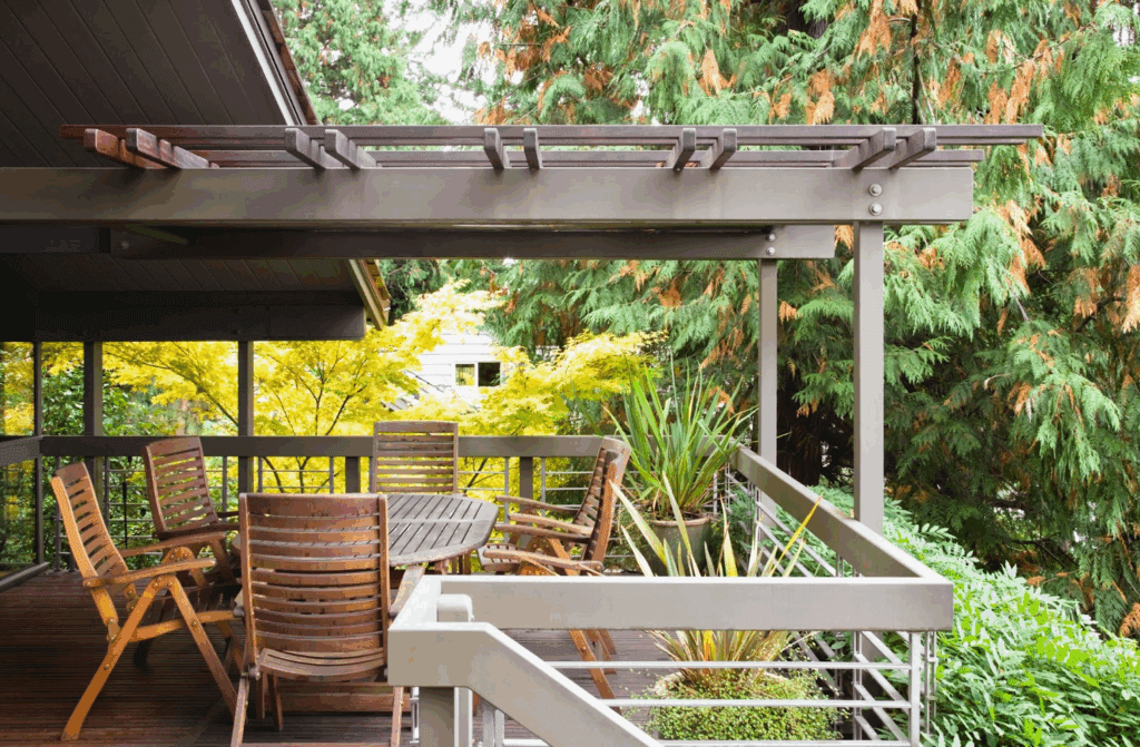 A backyard deck surrounded by greenery is shaded by a patio cover.