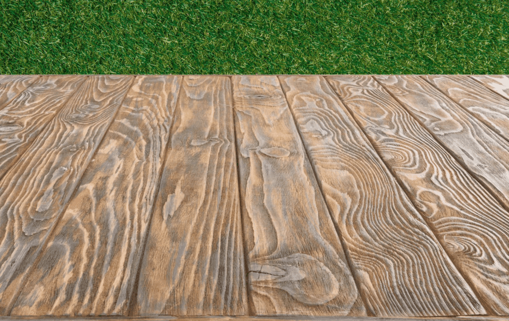 The edge of a wood grain vinyl deck with grass in the background.