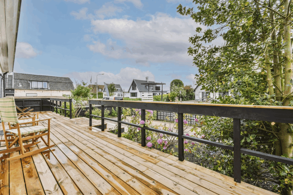 A wooden outdoor deck with custom black and wood railing in front of a garden.