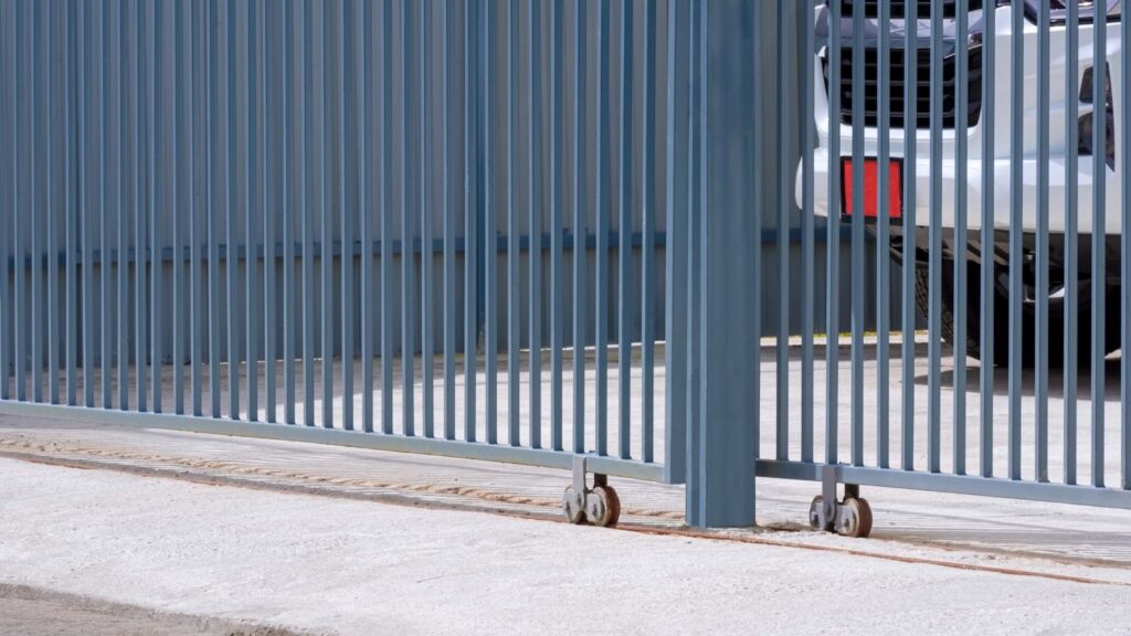 Side view of a sliding metal fence gate at a residential driveway with a car parked inside